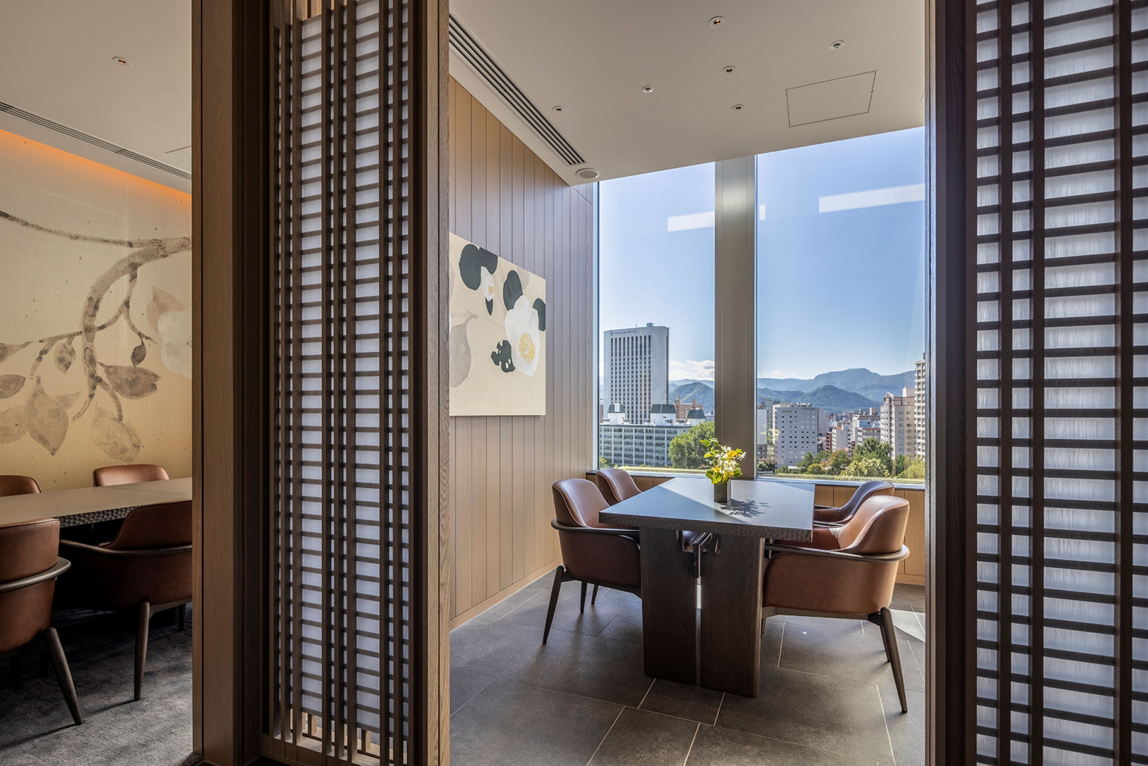 A modern dining area with a large table and chairs, a city view through large windows, and a decorative wall piece.