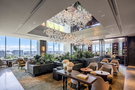 A spacious lobby with a high ceiling, large windows, and a view of the city. There are seating areas, a bar, and a reception desk.