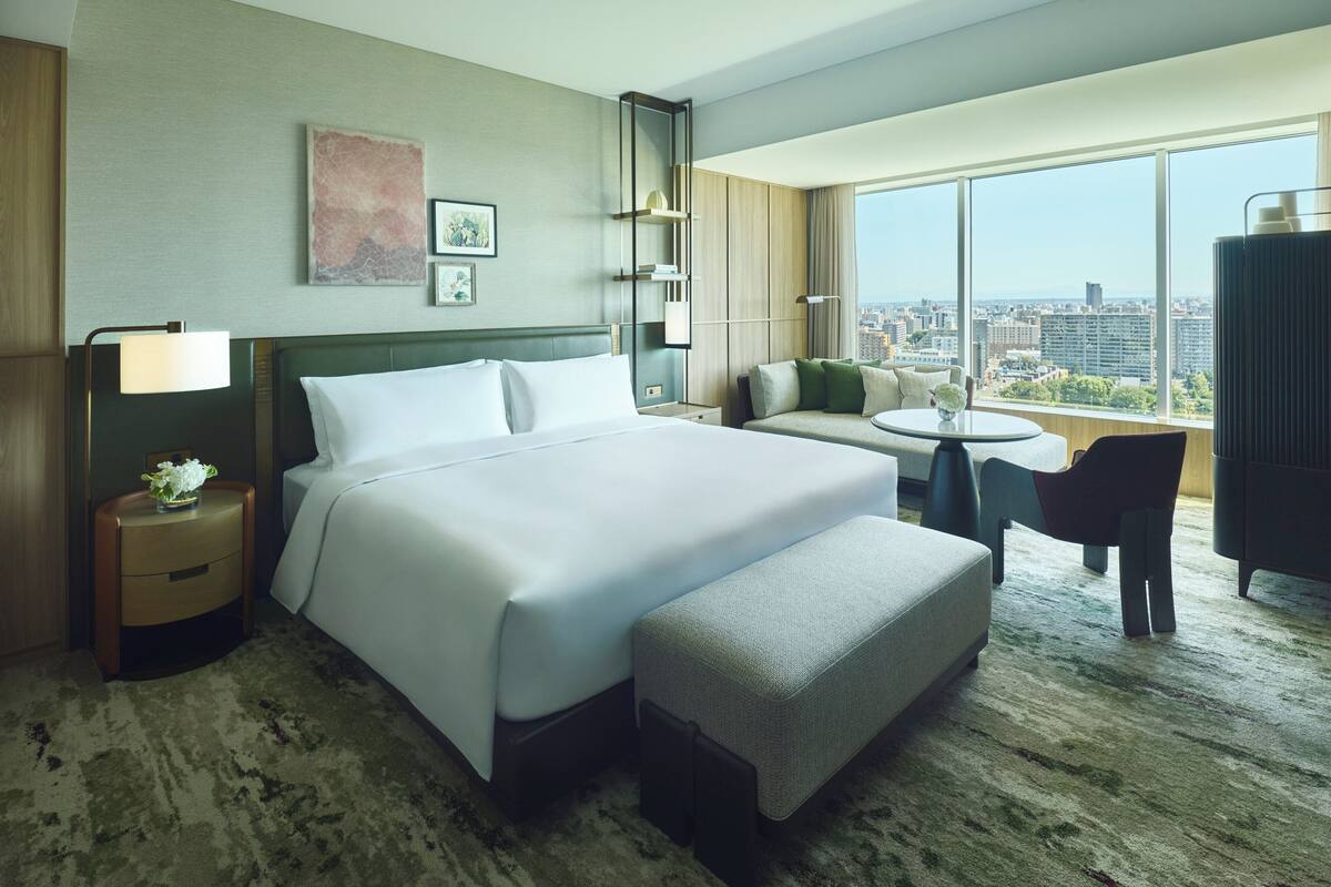 A hotel room with a large bed, a sofa, a small table, and a view of the city.