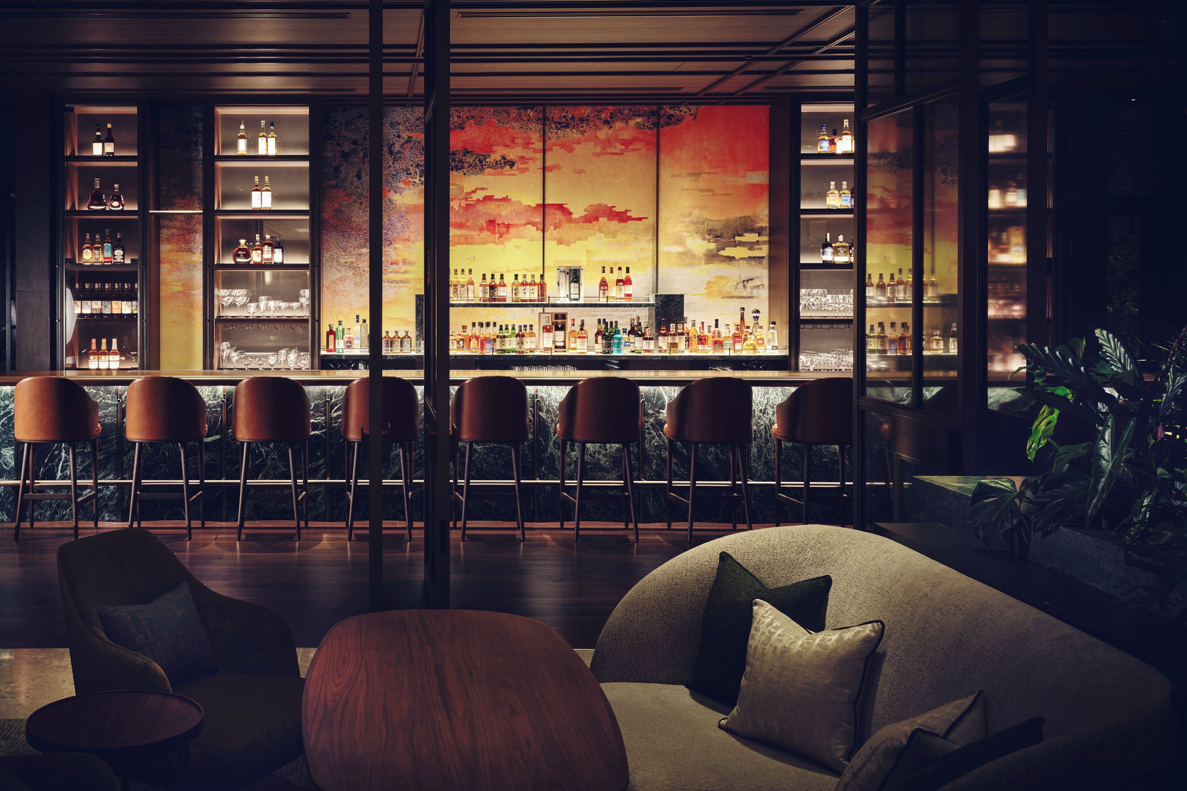 Uma área de bar com um grande mural, banquetas e prateleiras cheias de garrafas.