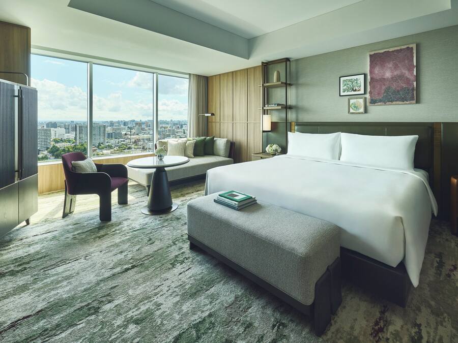 Ein modernes Hotelzimmer mit einem großen Bett, einer Couch, einem kleinen Tisch und Blick auf die Stadt.