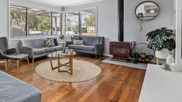 A living room with a grey sofa, armchairs, a coffee table, a fireplace, and a large window with blinds. - Bellarine Beach Shack (St Leonards)