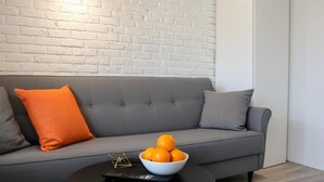 A modern living room with a grey sofa, a round black coffee table, and a bowl of oranges.