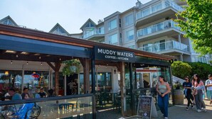 Un café llamado 'Muddy Waters Coffee + Kitchen' con mesas al aire libre y vistas a edificios residenciales al fondo.