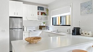 A modern kitchen with white cabinetry, a built-in stove, a refrigerator, and a large island with stools. - Town & Tide, Cowes Central (Cowes)