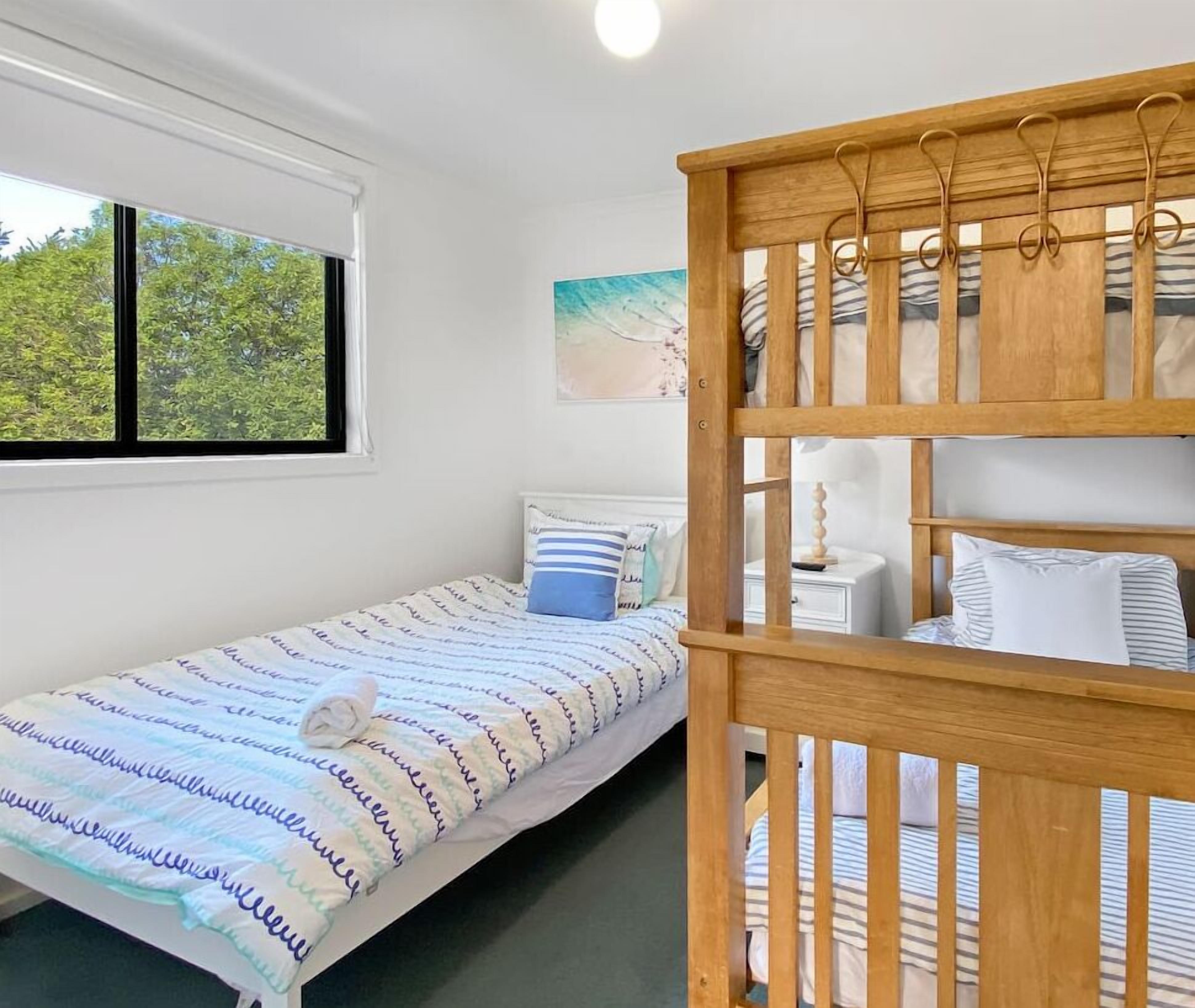Ein Schlafzimmer mit Etagenbett, einem Einzelbett, einem Fenster mit Blick auf Bäume und einem Bild an der Wand.
