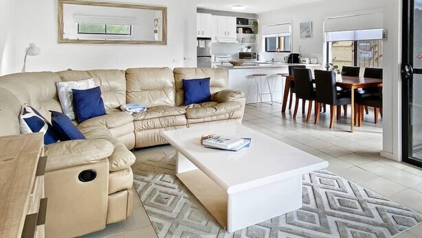 A modern living room with a beige sofa, a white coffee table, and a dining area with a wooden table and chairs. - Town & Tide, Cowes Central (Cowes)