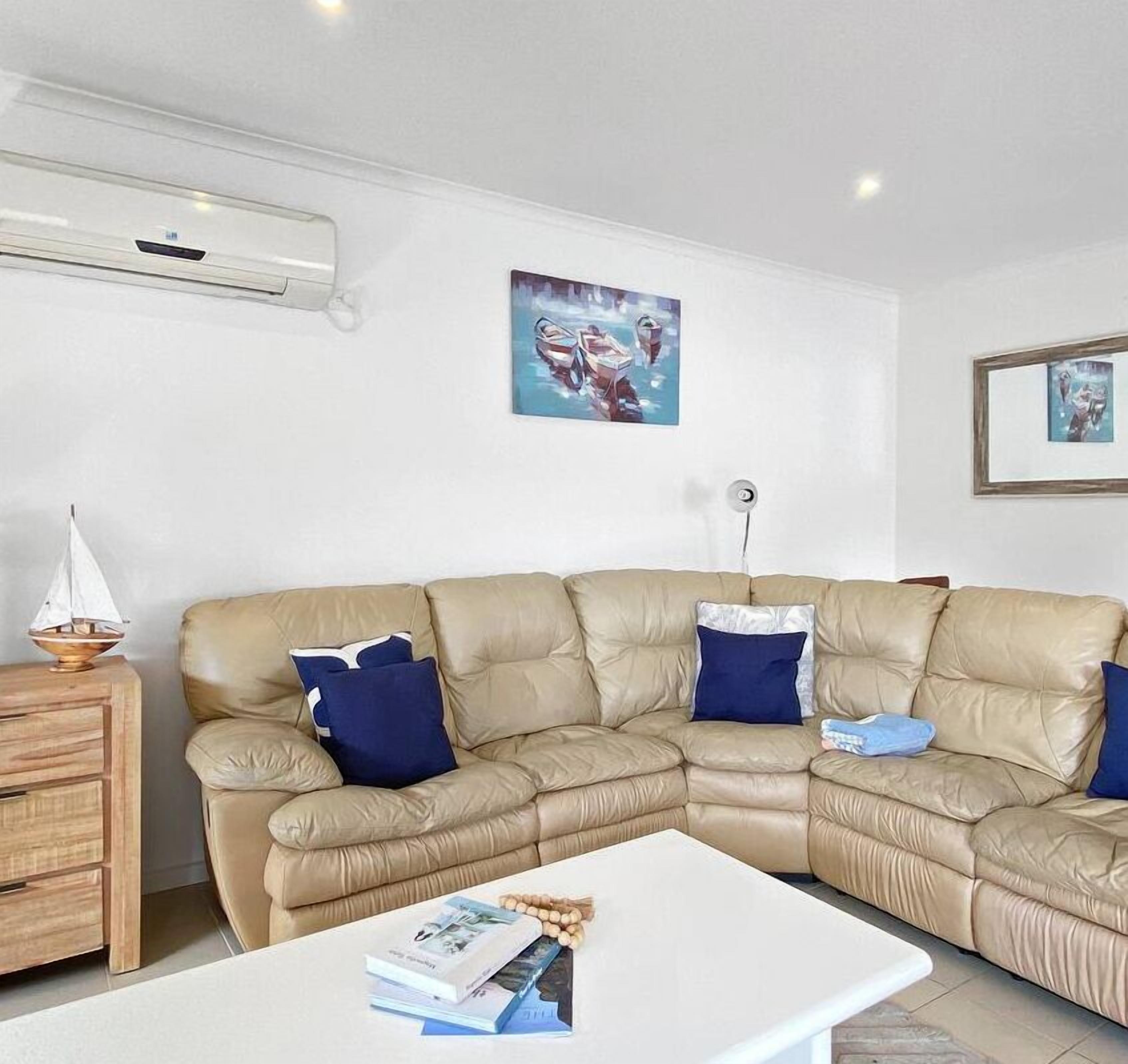 A modern living room with a beige sectional sofa, a white coffee table, and a wooden side table with a decorative item.
