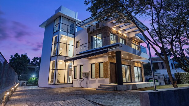 Une maison moderne à deux étages, dotée de grandes baies vitrées, d’un espace extérieur couvert et d’une allée pavée.