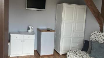 Una habitación con una cama, un televisor montado en la pared, un armario blanco y un mueble blanco pequeño.