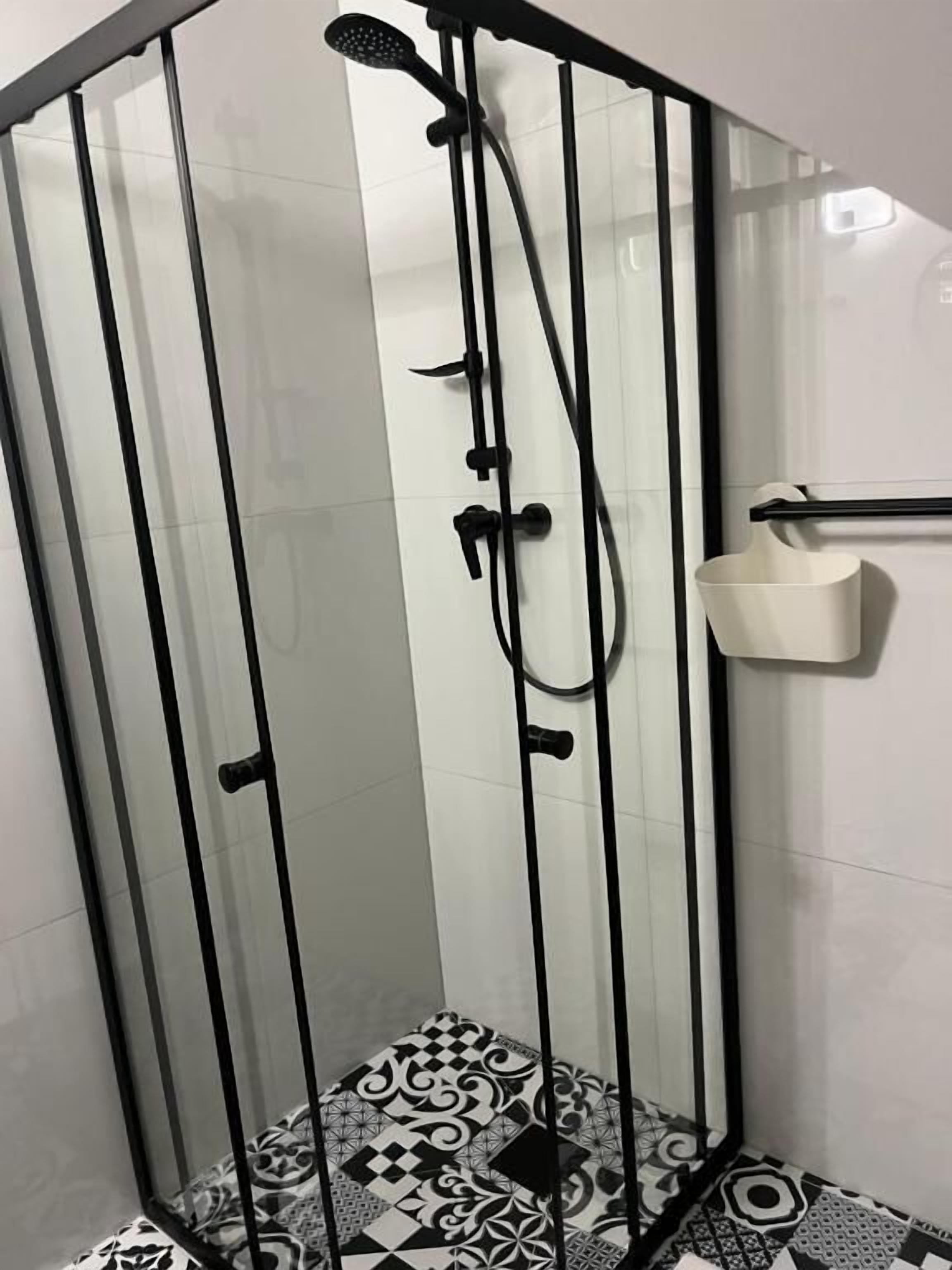 A glass-enclosed shower with a black metal frame, a handheld showerhead, and a wall-mounted faucet.
