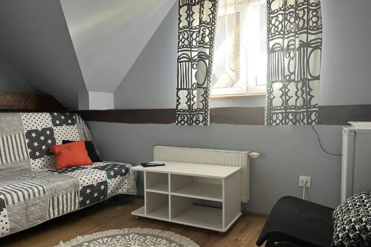 Ein Loft-Zimmer mit schrägem Dach, einem Sofa mit Patchwork-Bezug, einem weißen Konsolentisch und einem gemusterten Teppich.