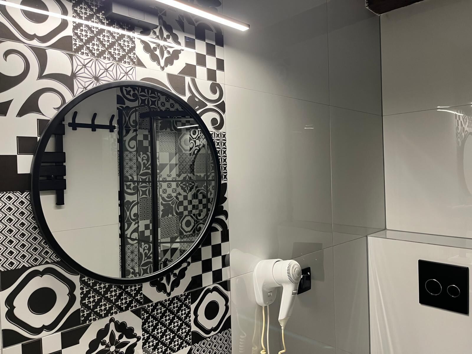 A bathroom with a round mirror, patterned tiles, a hairdryer, and a towel rack.