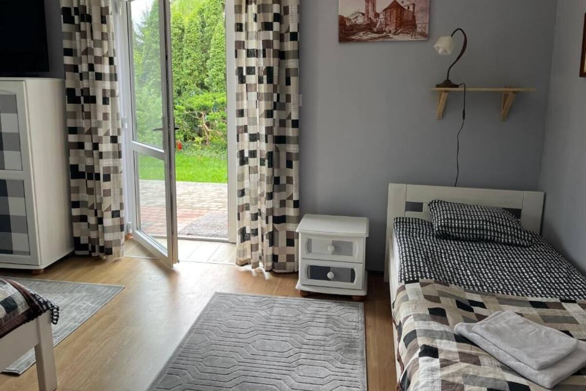 Ein Schlafzimmer mit einem Bett, einem Nachttisch, einem Schreibtisch, einem Stuhl, einem Fenster mit Vorhängen und einem Bild an der Wand.
