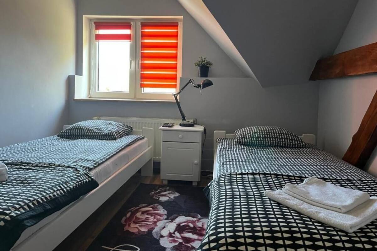 Ein Schlafzimmer mit zwei Betten, einem Fenster mit roten Jalousien, einem Schreibtisch mit Lampe und einer Heizung.