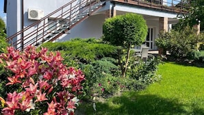 Ein zweistöckiges Haus mit Balkon, Treppe und einem gepflegten Garten mit verschiedenen Pflanzen und Blumen.