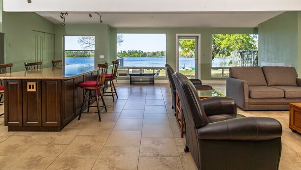 Amplia sala de estar con isla de cocina, taburetes de bar, sofá y vista a un lago.