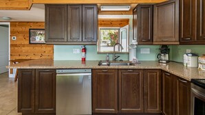 Una cocina con armarios de madera, encimera de granito, lavavajillas, fregadero y cafetera.