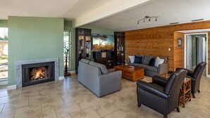 Un salón amplio con chimenea, sofás grises, sillones de cuero y una pared de acento de madera.