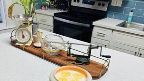 Une cuisine avec des meubles blancs, un four à micro-ondes, une cuisinière et un plateau en bois sur lequel se trouvent une bougie et une balance.