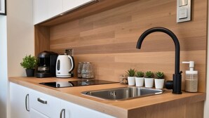 Eine moderne Küche mit einer Holzarbeitsplatte, einer Edelstahlspüle und einem schwarzen Wasserhahn. Auf der Arbeitsplatte stehen kleine Topfpflanzen und eine Kaffeemaschine.