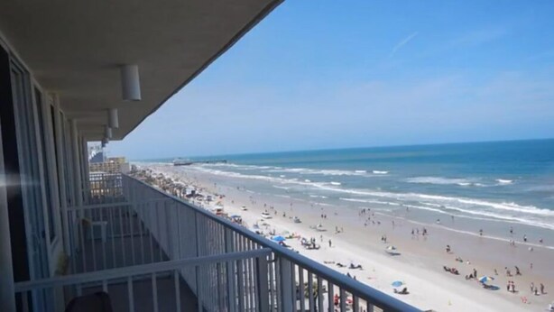 A balcony overlooking a beach with people and umbrellas. - Breathtaking, Oceanfront 6th Floor Condo, 2-bath, sleeps up to 4 (Daytona Beach)