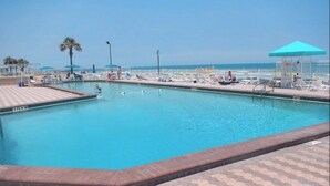 A swimming pool with a tiled deck, lounge chairs, and umbrellas. - Breathtaking, Oceanfront 6th Floor Condo, 2-bath, sleeps up to 4 (Daytona Beach)