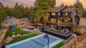Una casa grande con cancha de baloncesto, mobiliario exterior y un mural.