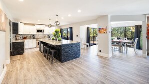 Cocina amplia con una isla grande, armarios blancos y vistas a un área de comedor exterior.
