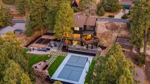 Una casa grande con un amplio patio trasero, que incluye una cancha de tenis y una zona de estar al aire libre.