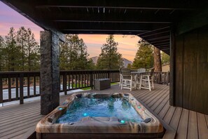 Un jacuzzi en una terraza de madera con vistas a árboles y montañas.