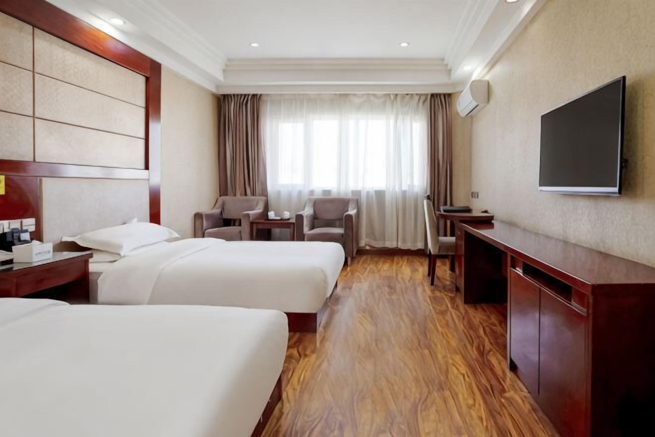 Ein Hotelzimmer mit zwei Betten, einem Fernseher, einem Schreibtisch und einer Sitzecke.