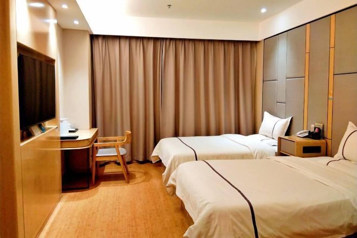 Ein Hotelzimmer mit zwei Betten, einem Schreibtisch, einem Sessel, einem Fernseher und einem großen Fenster mit Vorhängen.