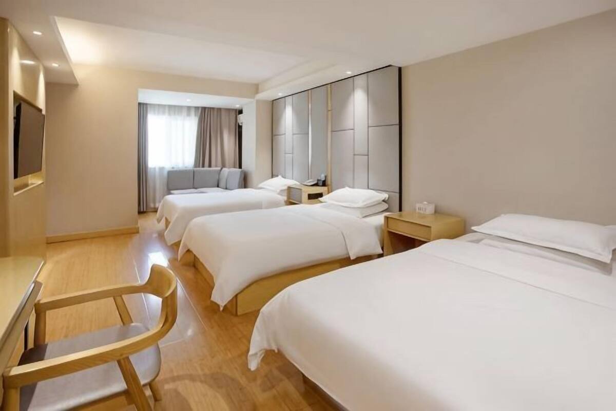 Ein Hotelzimmer mit drei Betten, einem Schreibtisch, einem Stuhl und einem großen Spiegel.