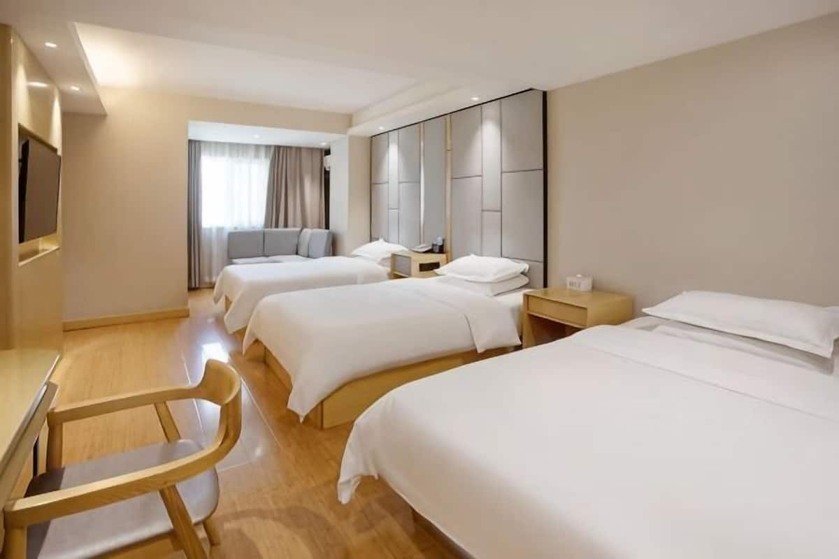 A hotel room with three beds, a desk, a chair, and a large mirror.