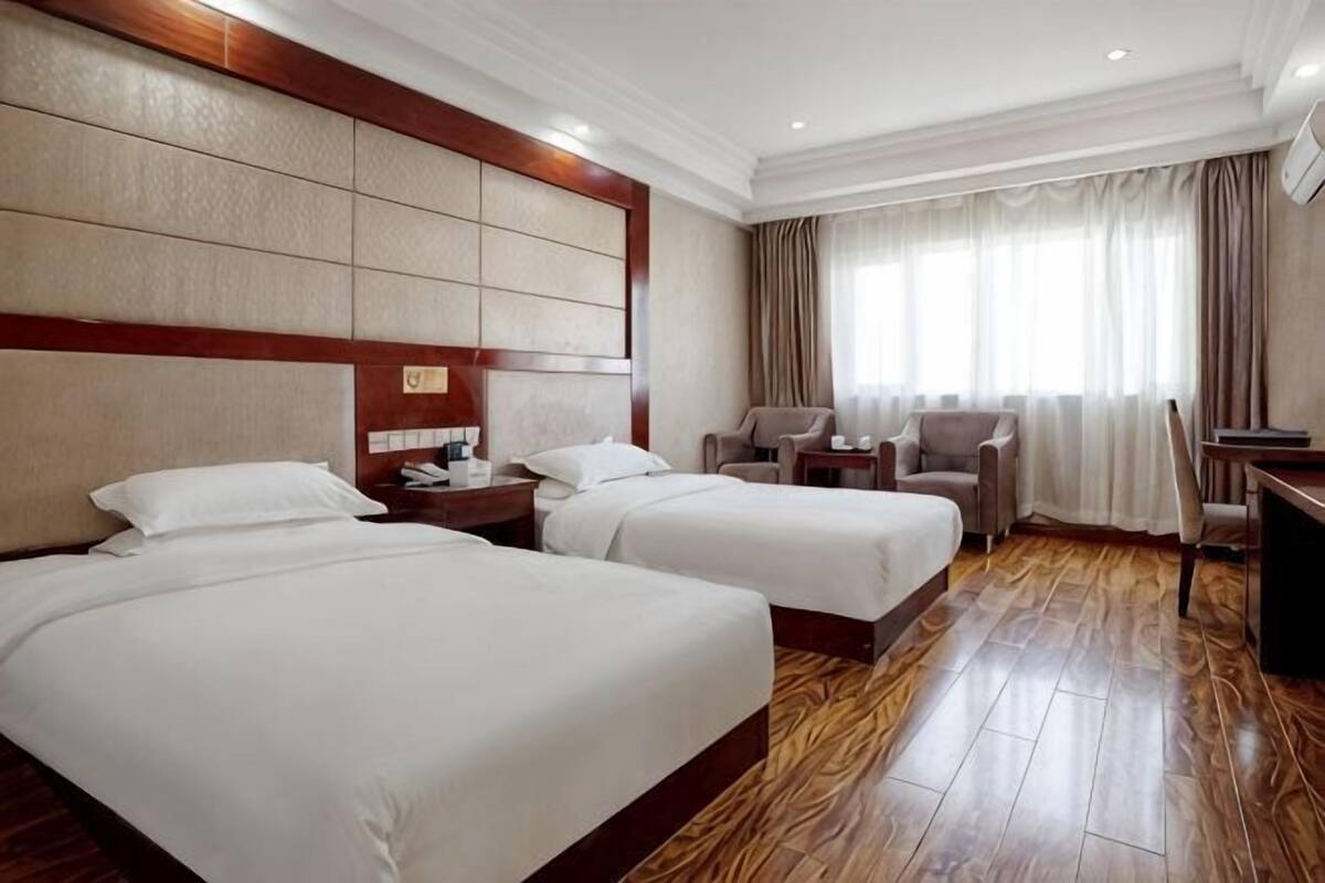 Ein Hotelzimmer mit zwei Betten, einem Schreibtisch, einem Sessel und einem Fernseher.