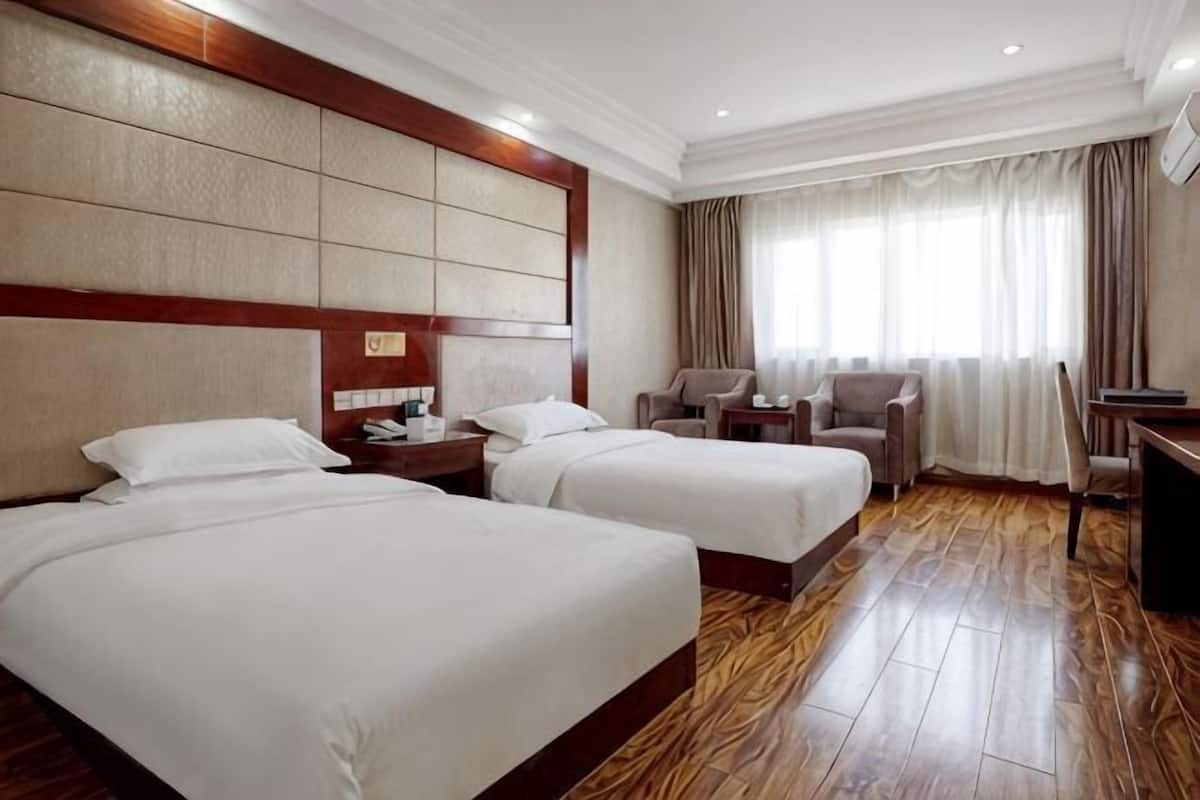 A hotel room with two beds, a desk, a chair, and a TV.
