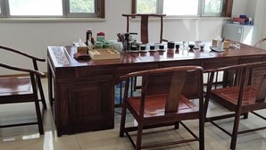 Een eetgedeelte met een houten tafel en stoelen, een klein kastje en een raam met uitzicht op groen.