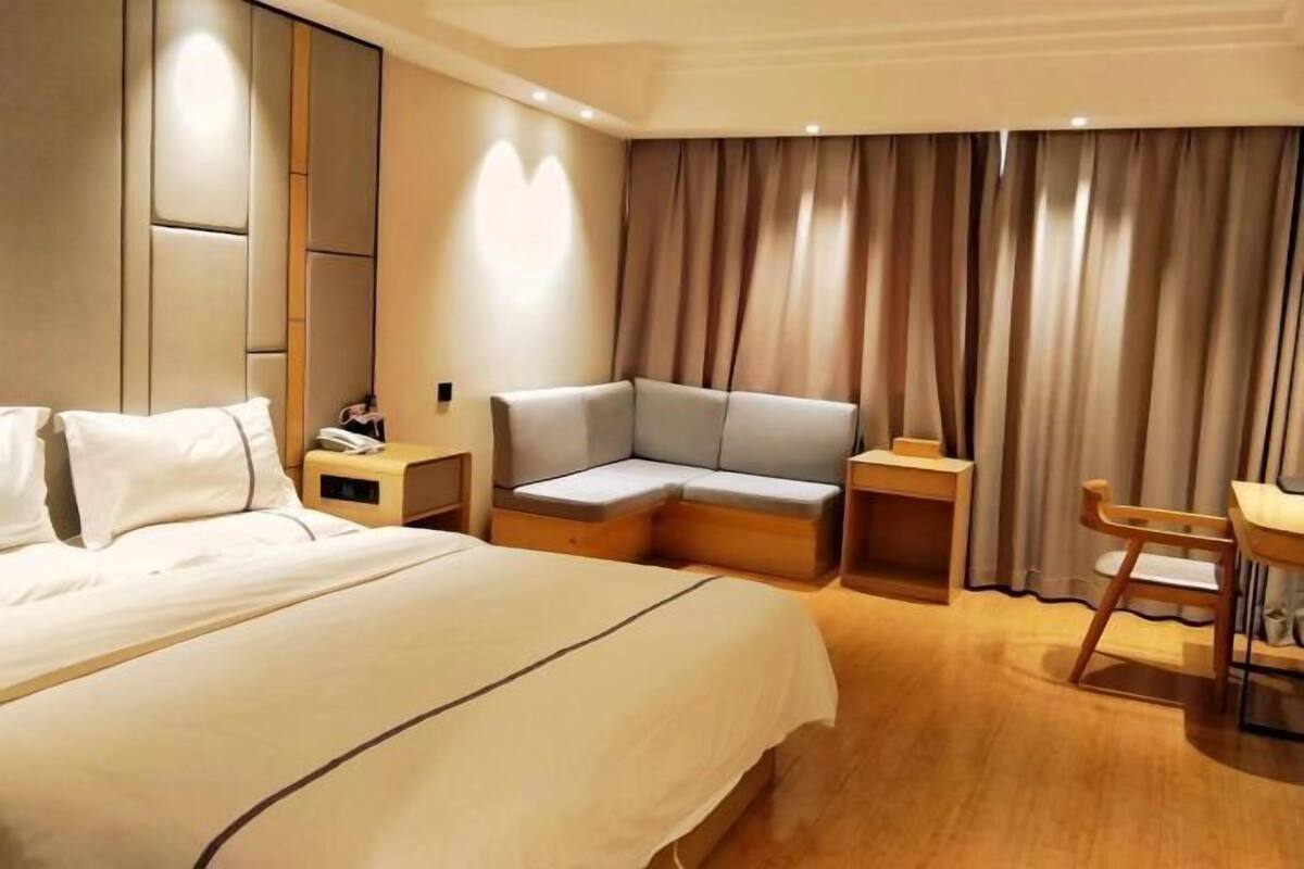 Ein Hotelzimmer mit einem großen Bett, einer Sitzecke, einem Schreibtisch und einem fenster mit Vorhängen.