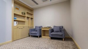 Een kleine, knusse kamer met twee grijze fauteuils, een houten kast met planken en een kamerbreed tapijt met dessin.