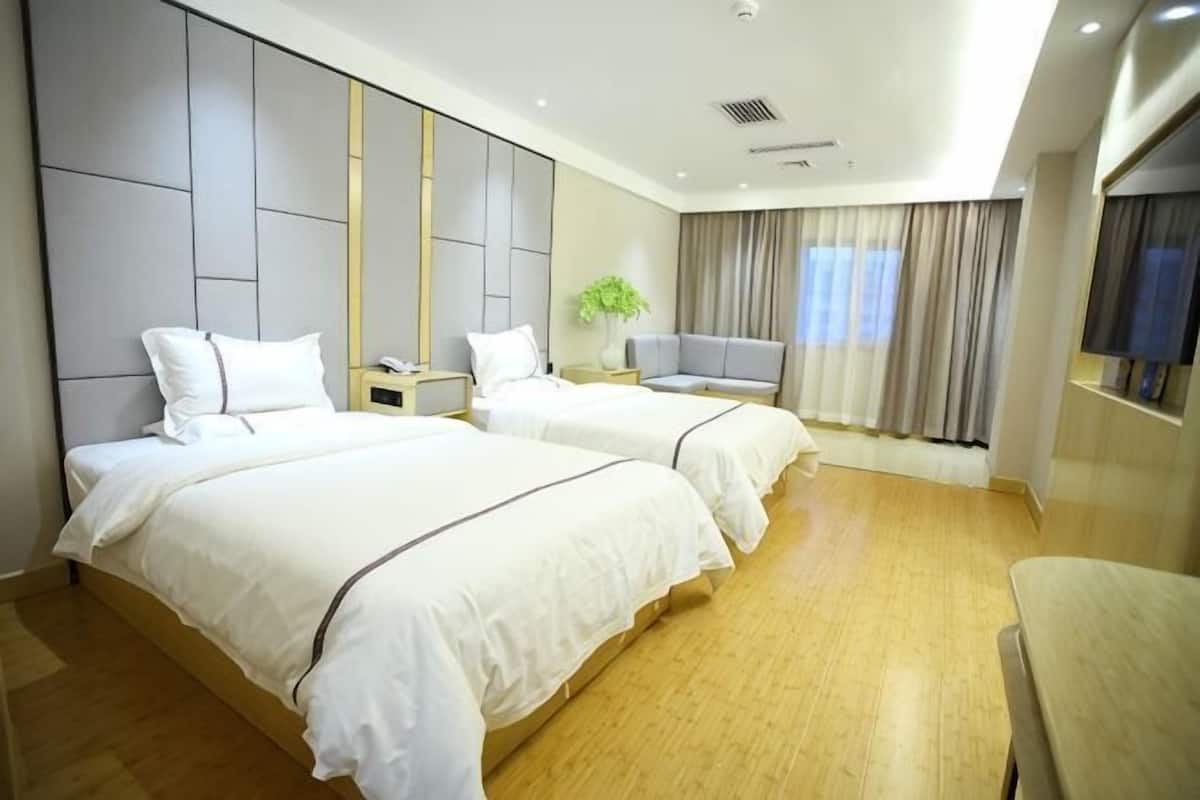 A hotel room with two beds, a desk, a chair, and a TV.