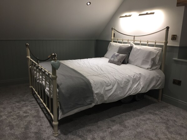 A bedroom with a bed, a headboard, a wall-mounted light, and a carpeted floor.