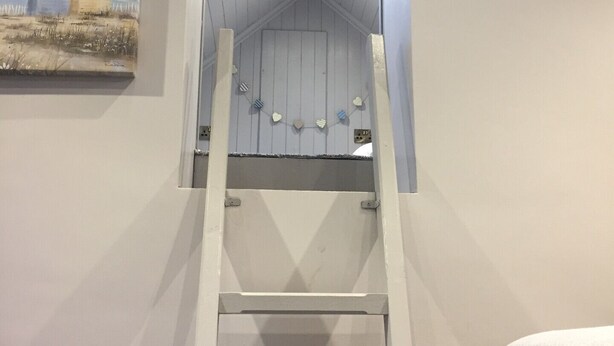 Una escalera blanca que lleva a un techo abovedado, un cuadro de cabañas de playa en la pared y una toalla en el suelo.