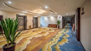 A hotel hallway with a patterned carpet, potted plants, and a reception desk. - Hua Xin Hotel Hengyang (Hengyang)