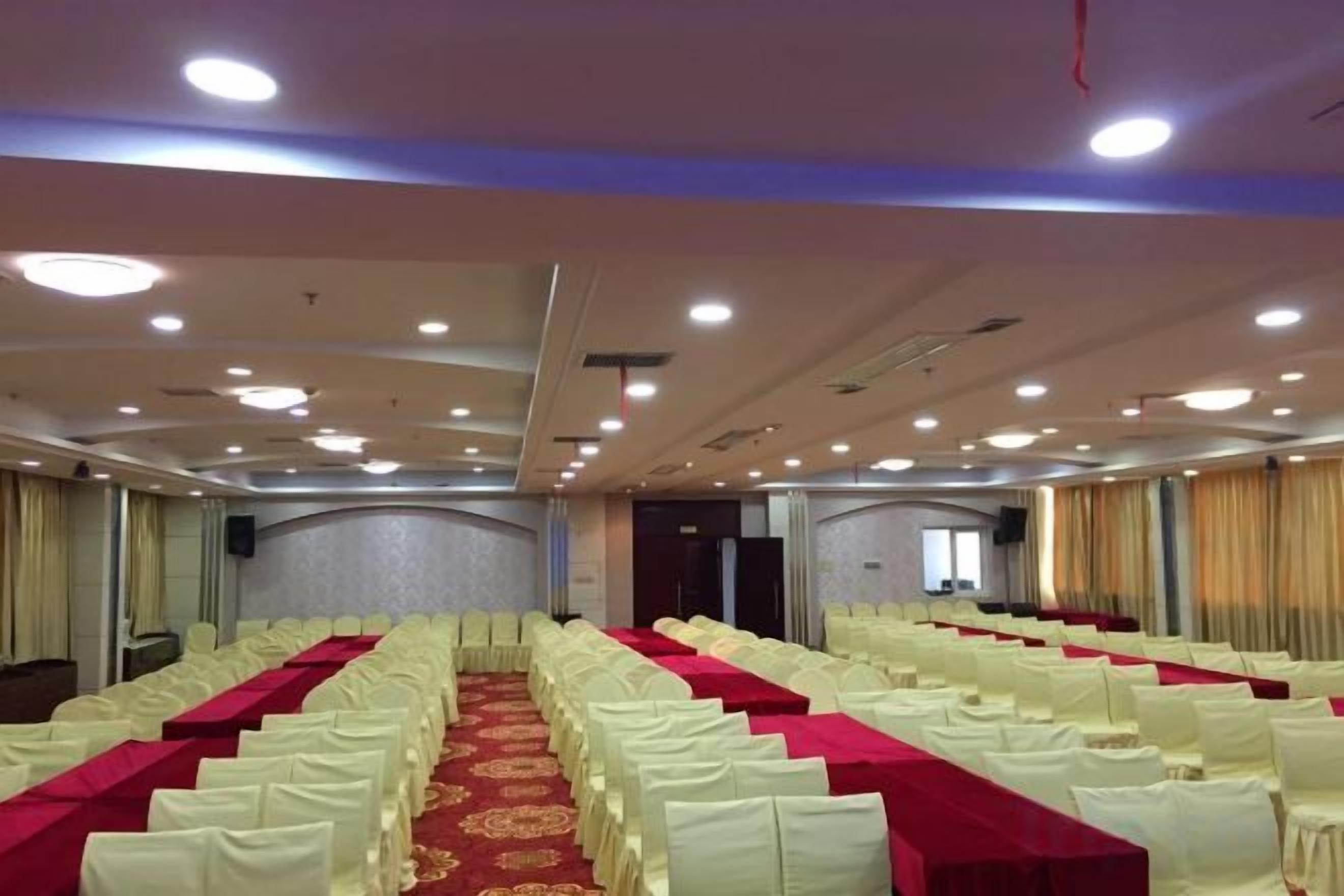 A conference room with rows of white chairs, a red carpet, and a stage at the front.