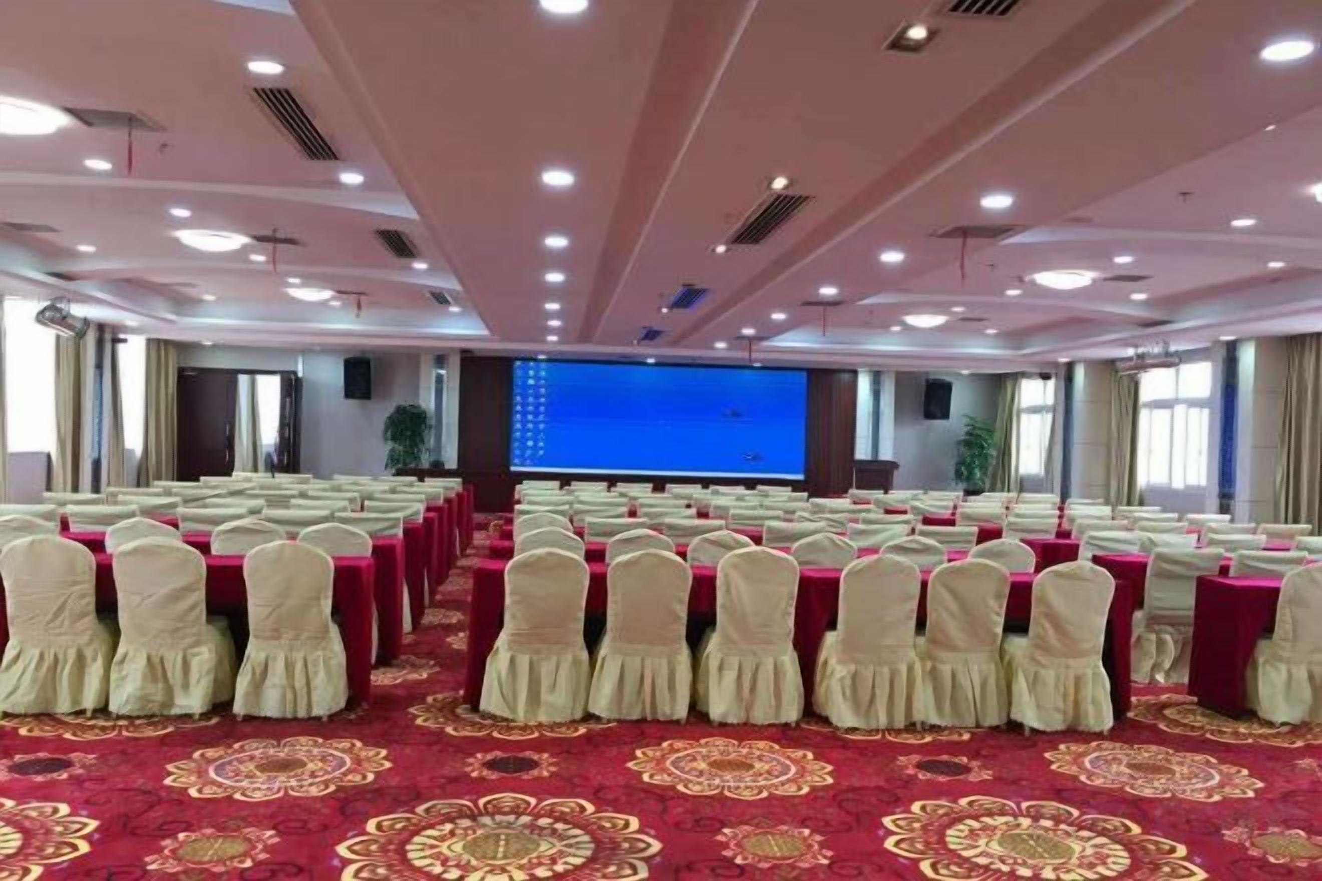 A conference room with rows of tables and chairs, a large screen, and a patterned carpet.