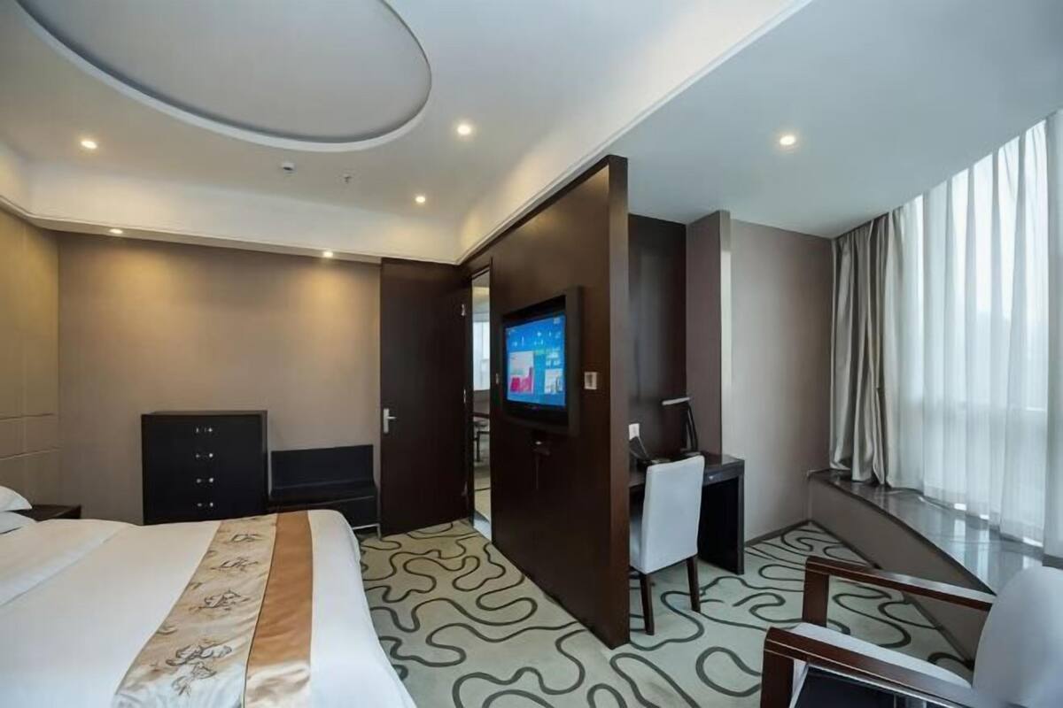 A hotel room with a bed, a desk, a television, and a large window.