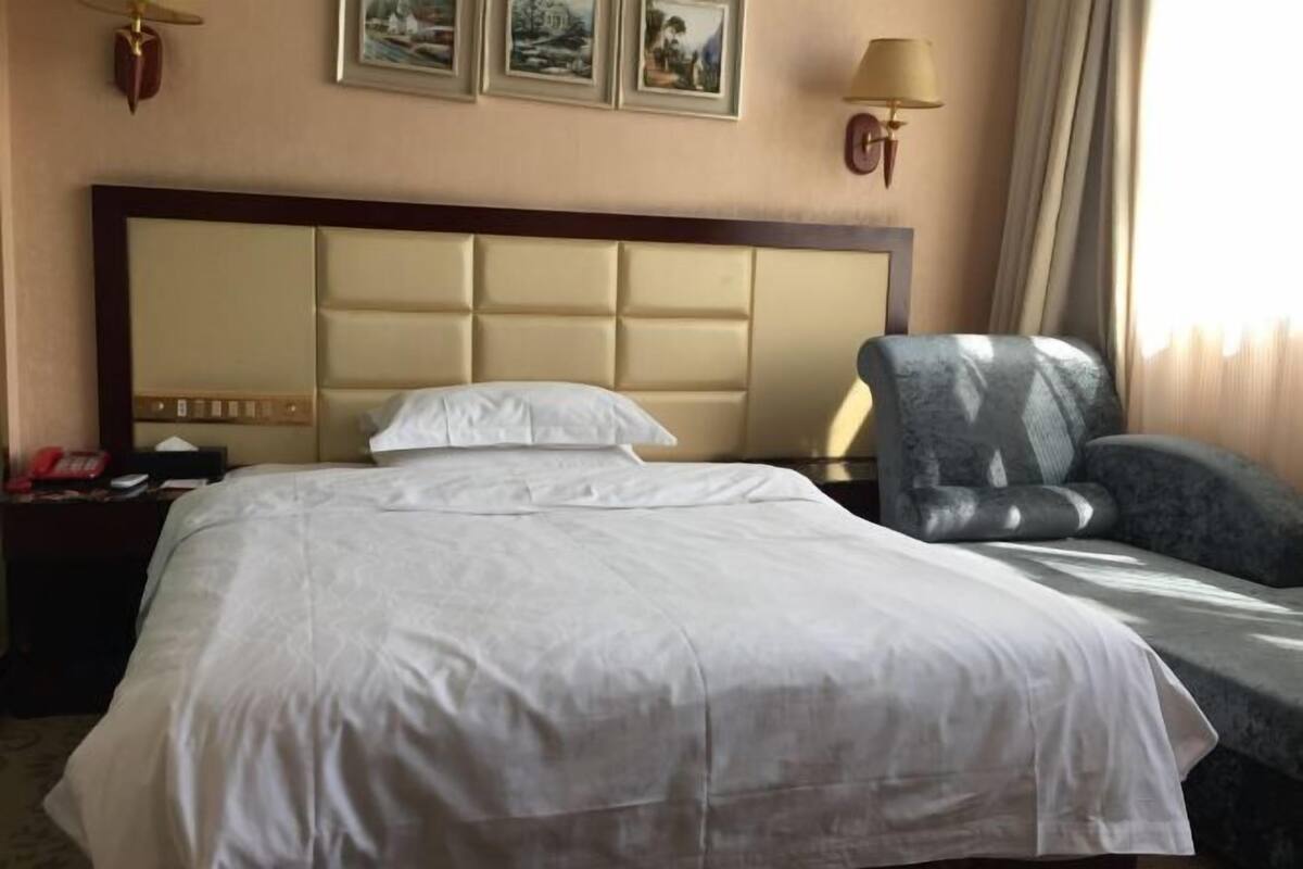 A hotel room with a large bed, a chair, a nightstand with a phone, and wall-mounted lamps.