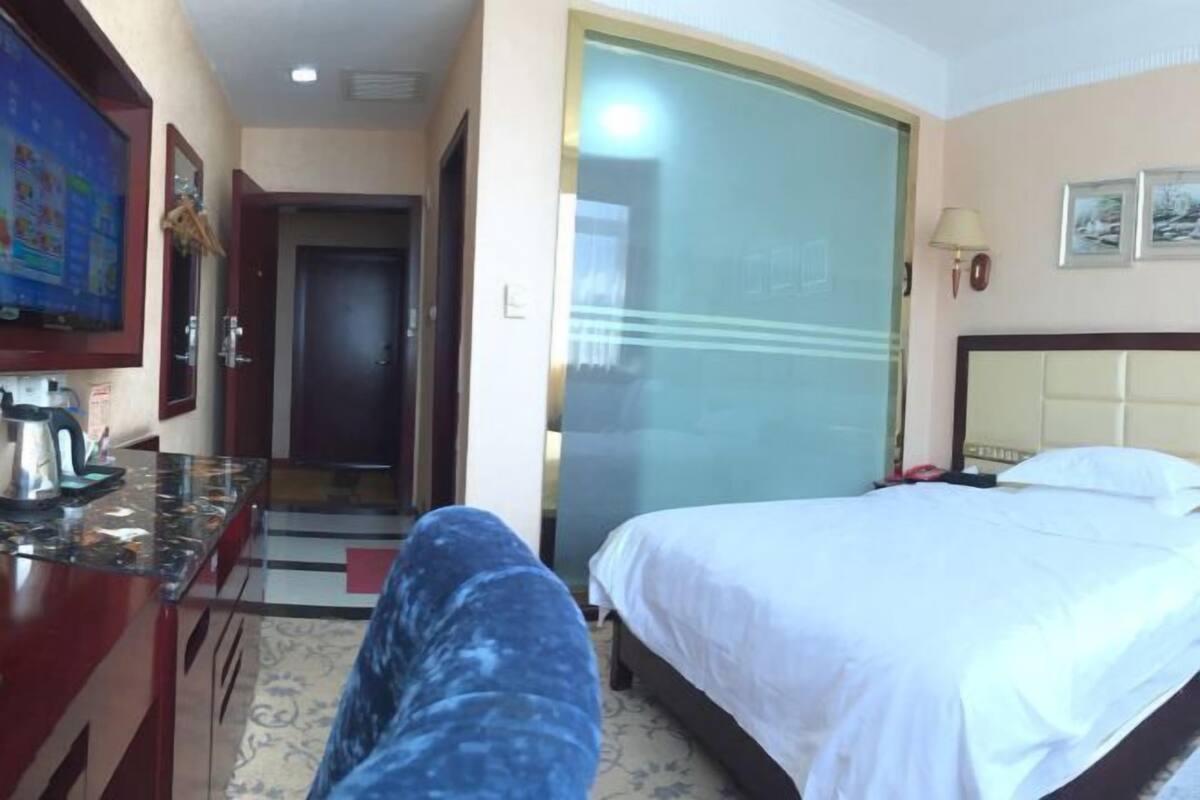 A hotel room with a bed, a desk with a coffee maker, a television, and a door leading to another room.
