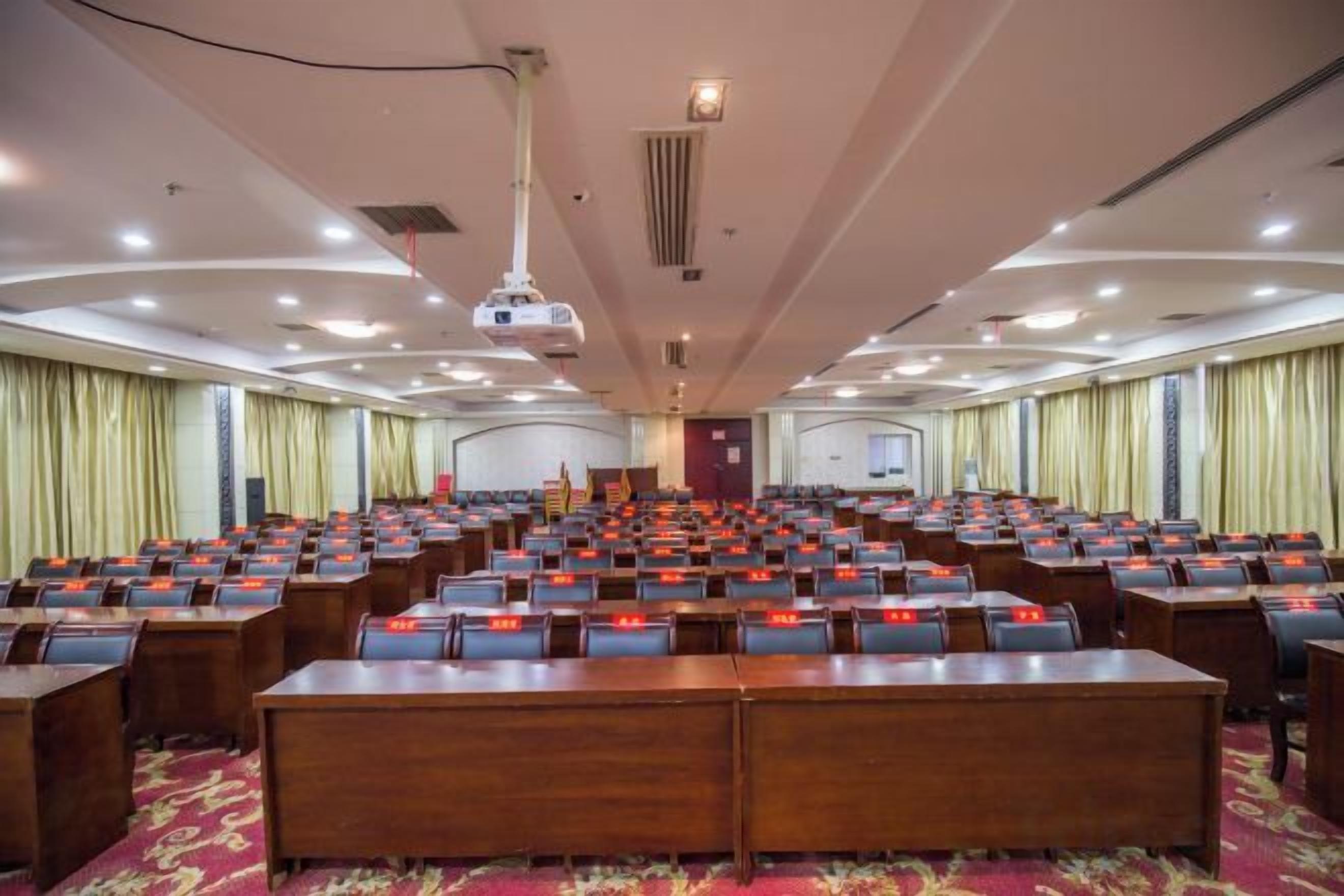 A conference room with rows of tables and chairs, a podium, and a projector.